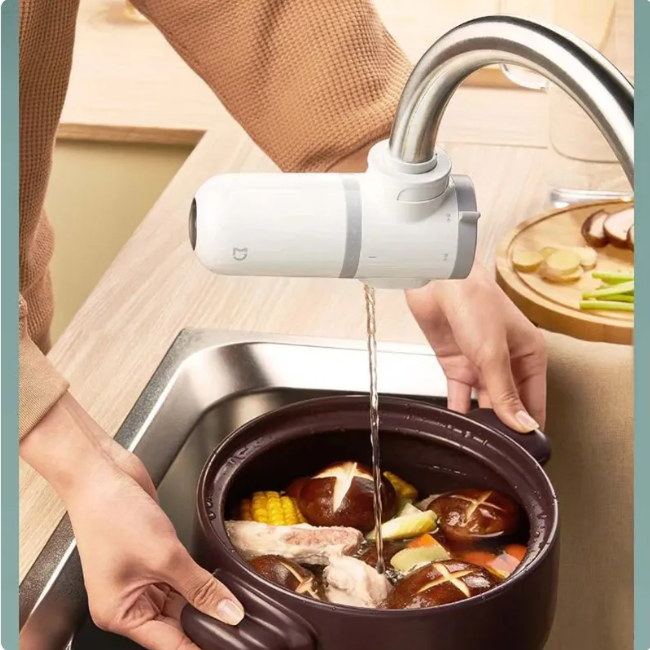 Person pouring water from a faucet into a pot of food on a kitchen counter.